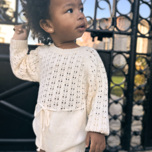 Bebé vistiendo un body de algodón crema con bordado artesanal y detalles en madera.